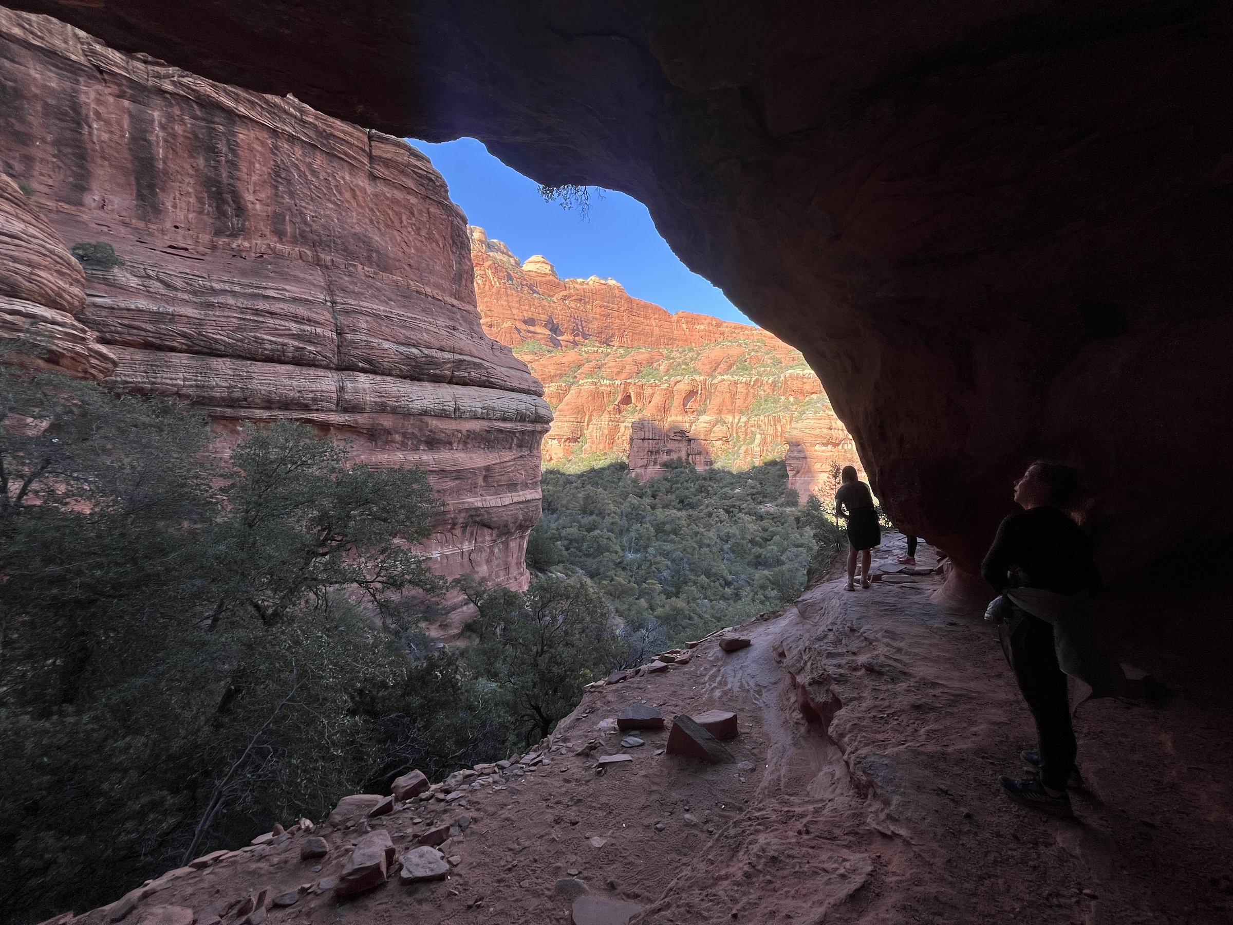 Hikers framed by a red rock cave arch