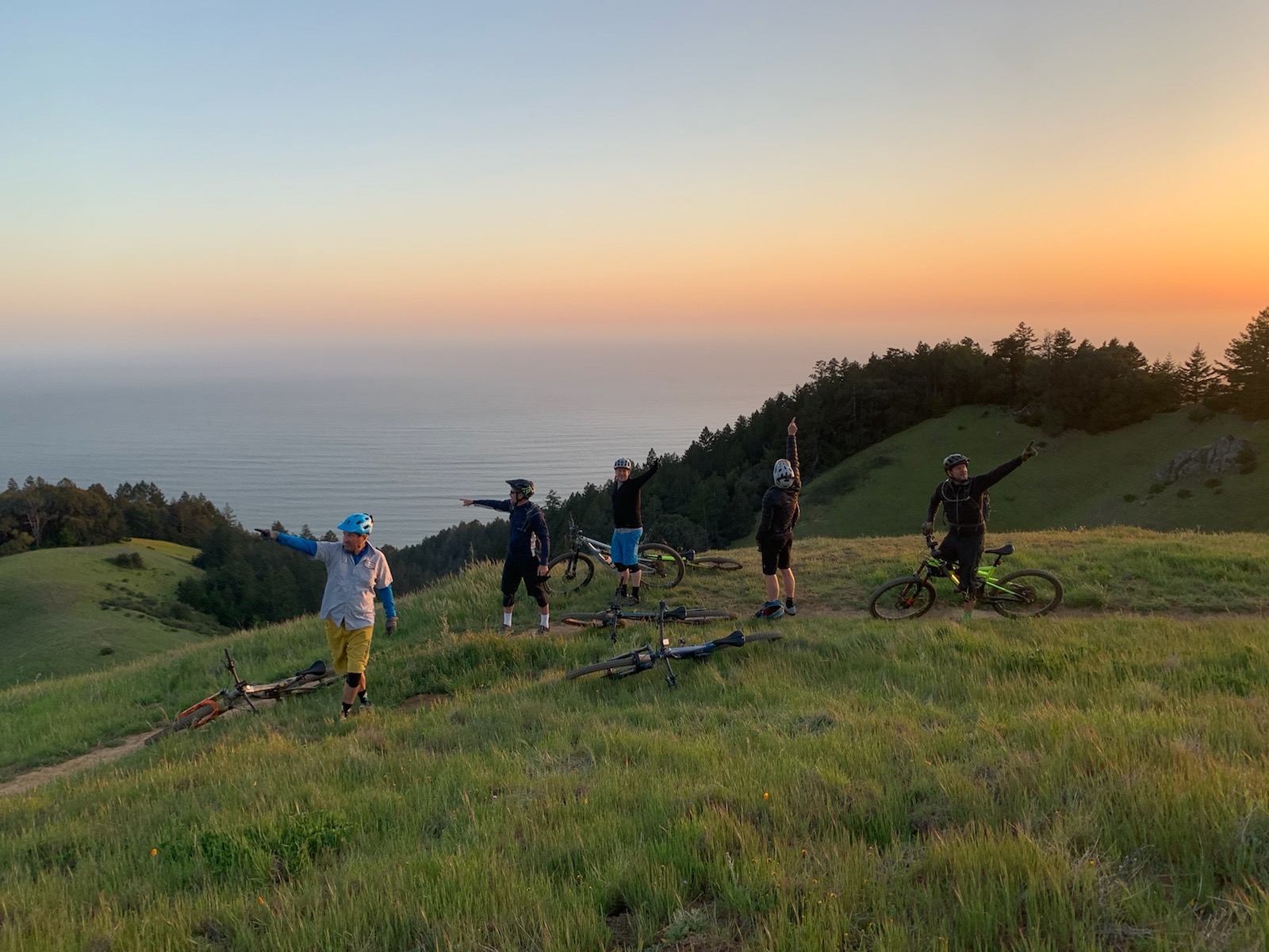Mountain bikers celebrating on a hilltop at sunset with ocean view